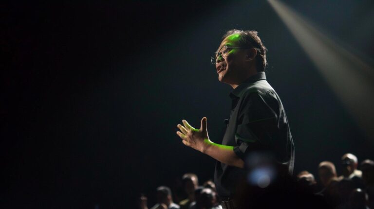 Man giving a presentation at a conference illuminated by stage lights.