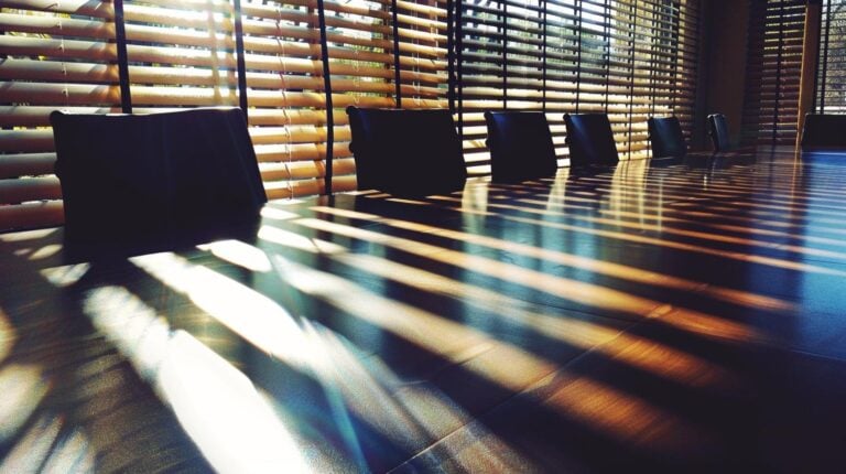 Modern office waiting area with chairs and sunlight casting shadows through blinds on the floor.