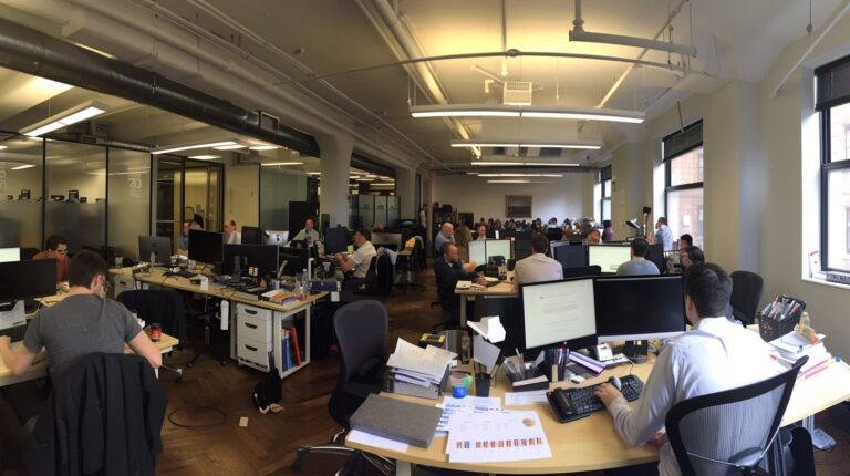 Open office space with people working at desks and computers modern workplace environment collaborative setting productivity team work technology business atmosphere natural light through windows
